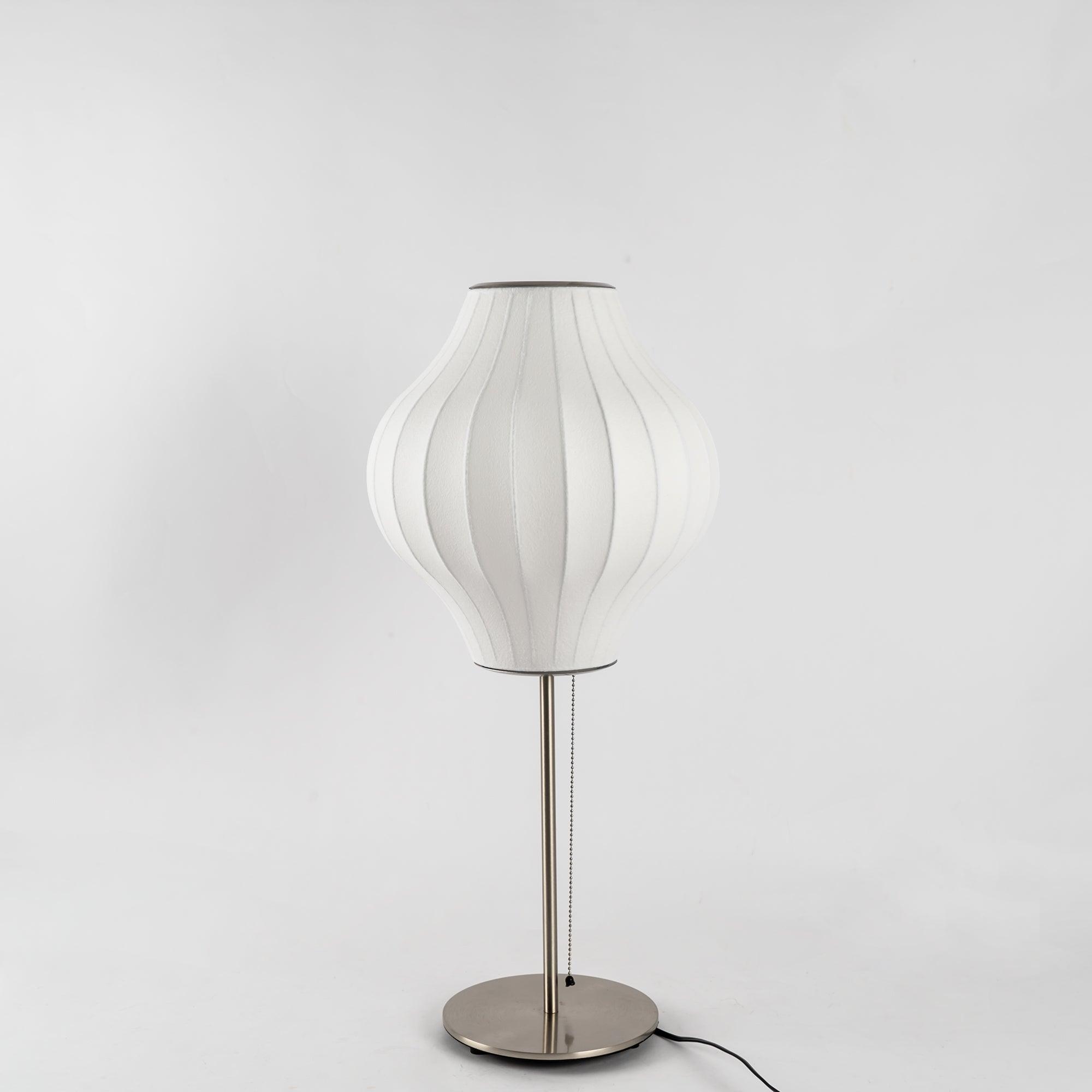 Faux silk bubble table lamp with chrome stem lit warmly on a side table