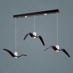 Three black bird-shaped pendants from this Clérachic fixture hang at staggered lengths from a black linear canopy.