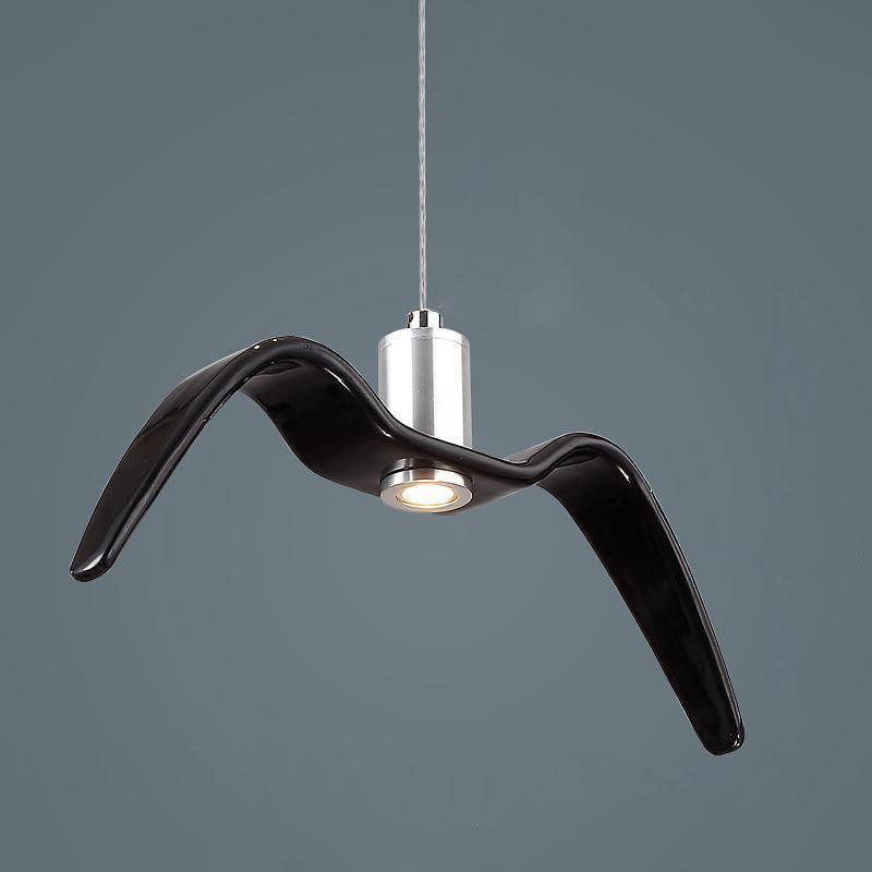 A black bird-shaped pendant from this Clérachic light hangs at an angle with its LED lit beneath one wing, on a dark blue-grey backdrop.