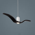 A black bird-shaped pendant from this Clérachic light is seen close, wings swept back with its LED lit, on a dark blue-grey backdrop.