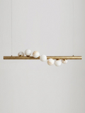 Product shot on a plain background: this Clérachic pendant's brushed brass bar hangs level on two thin cables, alabaster spheres clustered along it.