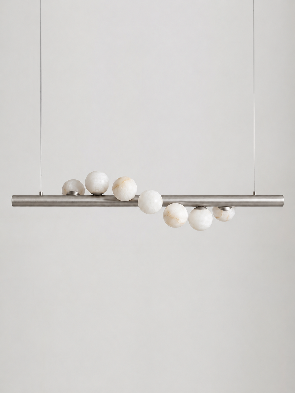 Studio shot on a bare background, this Clérachic pendant's brushed nickel bar holds alabaster spheres of varying sizes.