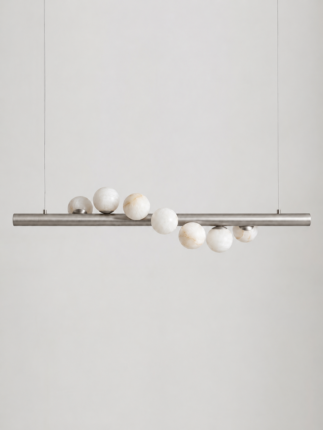 Studio shot on a bare background, this Clérachic pendant's brushed nickel bar holds alabaster spheres of varying sizes.