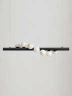 Studio shot on a bare background, this Clérachic pendant's matte black bar holds alabaster spheres clustered along its length.