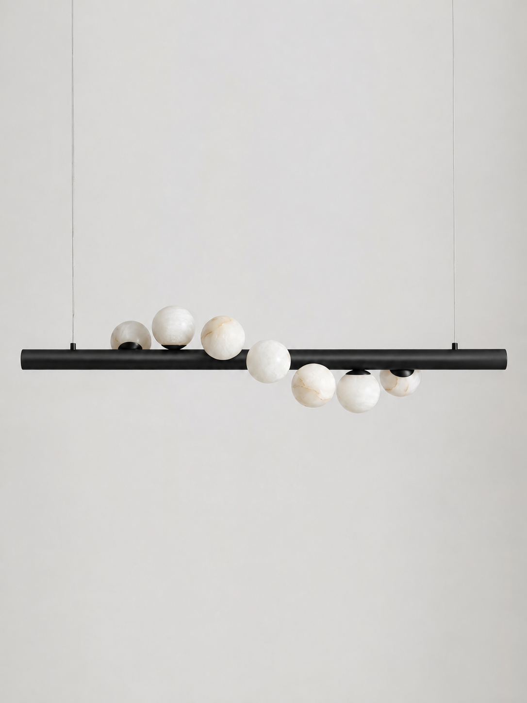Studio shot on a bare background, this Clérachic pendant's matte black bar holds alabaster spheres clustered along its length.