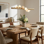 Above a wood table with a vase of white hydrangeas, this Clérachic pendant in brushed brass lights mismatched cream and white chairs.