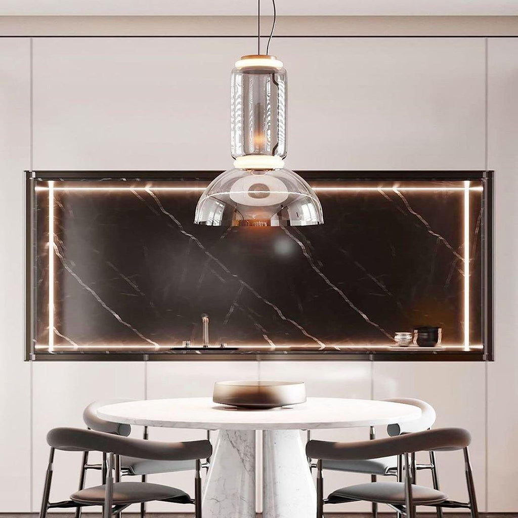 This Clérachic pendant hangs over a marble dining table in front of a black stone backsplash lit with a thin gold strip.