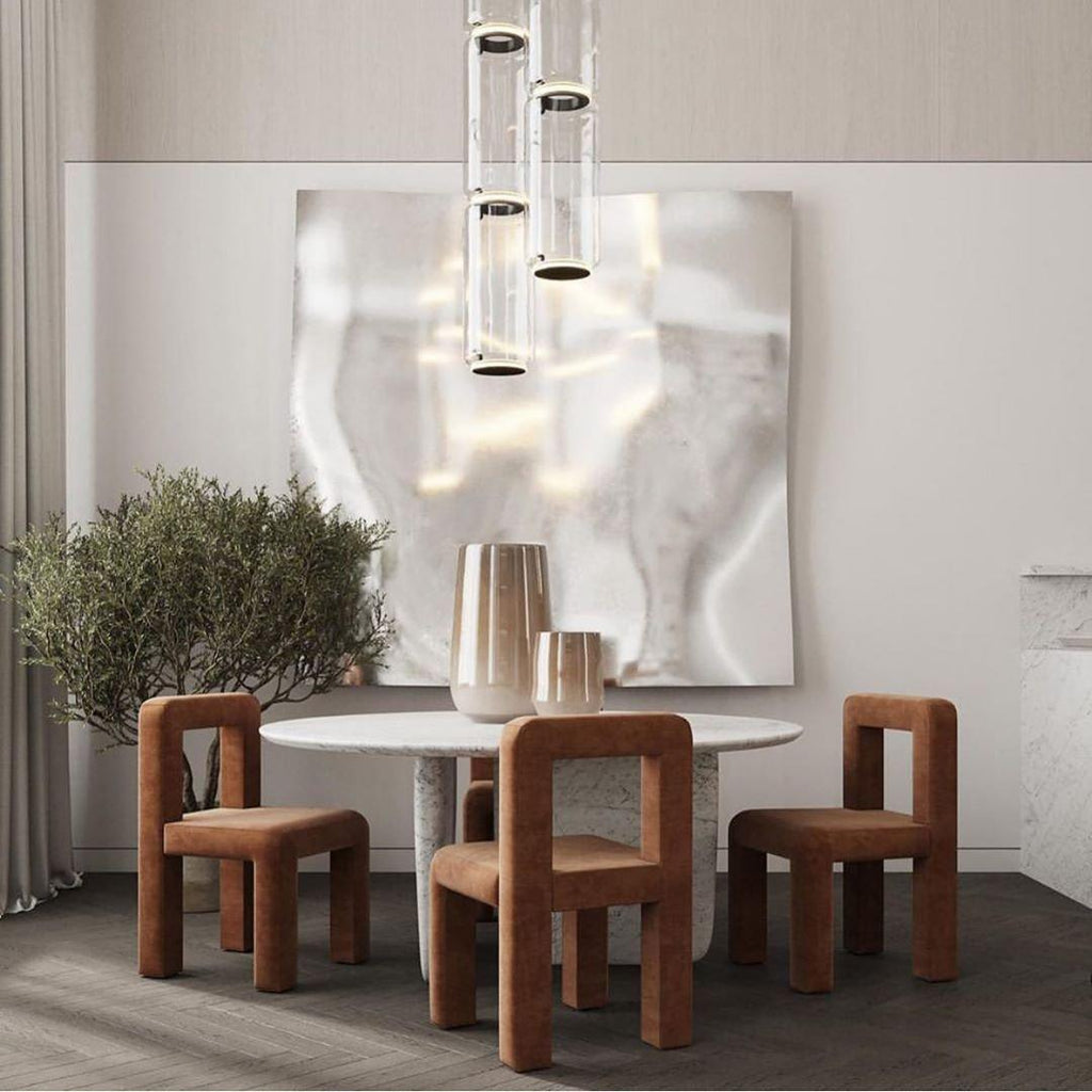 A three-cylinder cluster of this Clérachic pendant hangs above a round table beside a textured sculpture backdrop.
