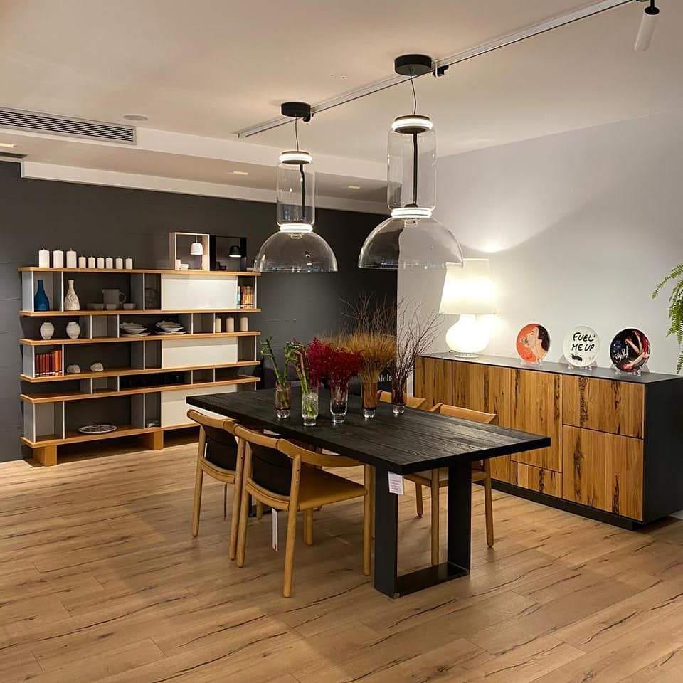 In a showroom, this Clérachic pendant hangs beside a dome-shaded companion above a dark wood table.