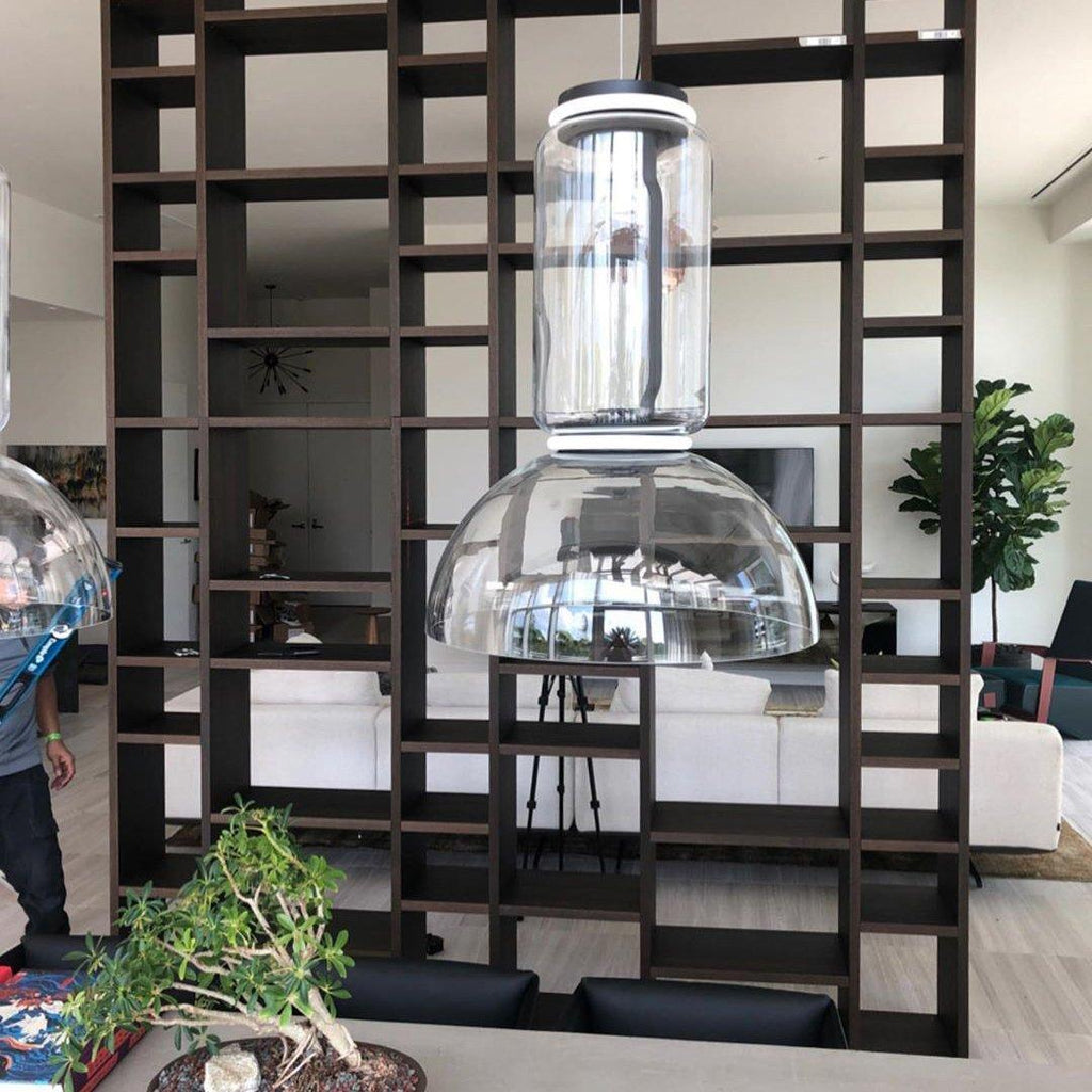 Close view of one dome-shaded Clérachic pendant hanging from an open shelving divider beside a potted plant.