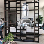 Close view of one dome-shaded Clérachic pendant hanging from an open shelving divider beside a potted plant.