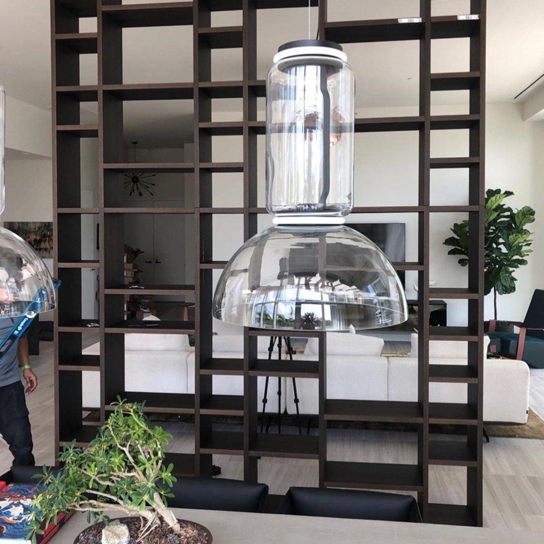 Close view of one dome-shaded Clérachic pendant hanging from an open shelving divider beside a potted plant.