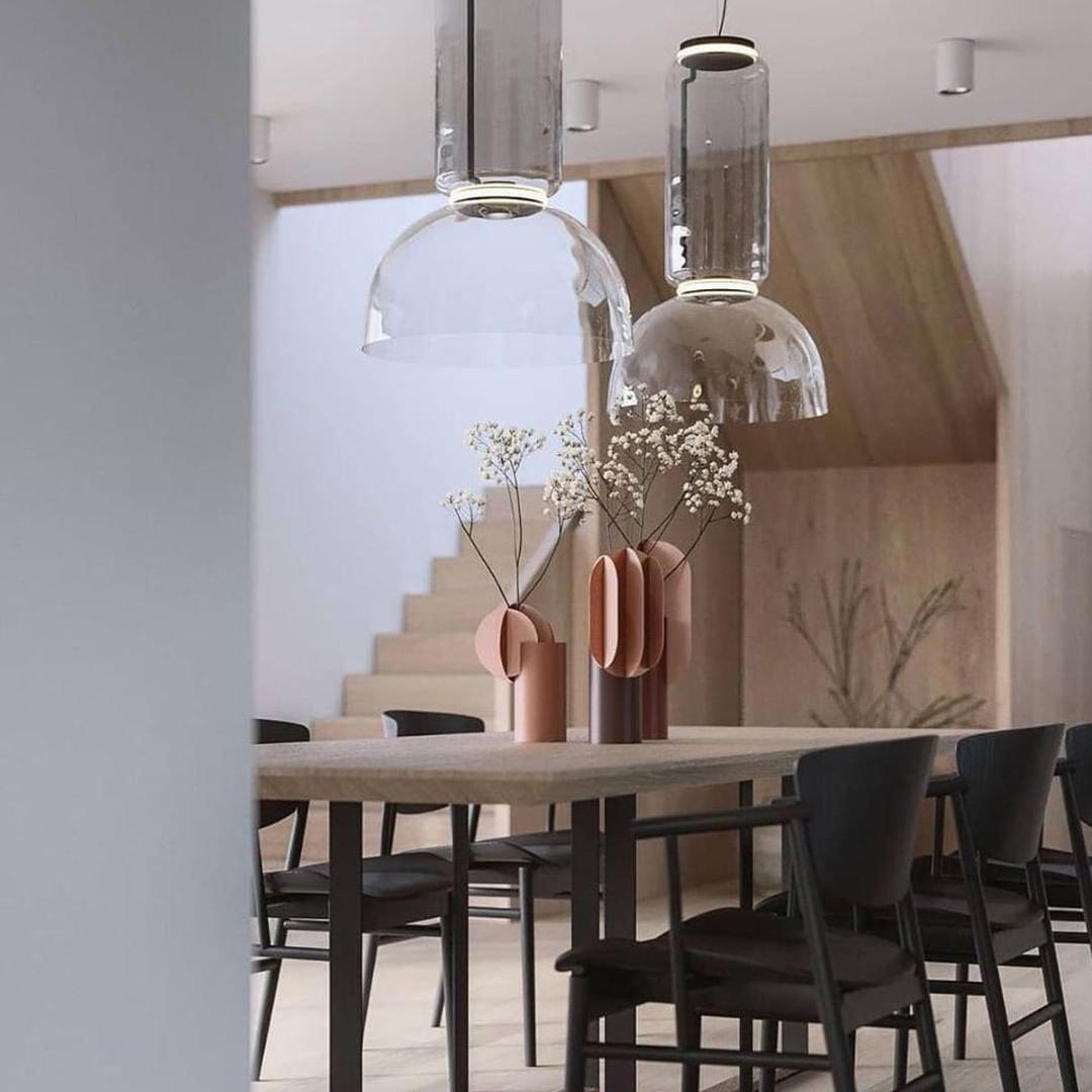 Two dome-shaded pendants from this Clérachic collection hang near a staircase above a wood dining table with pink vases.