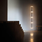 A tall single column of glowing cylinders from this Clérachic pendant lights a dark stairwell corner.
