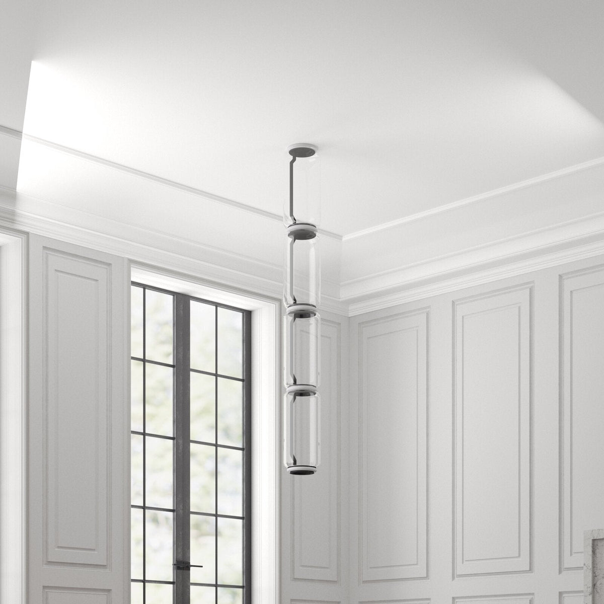 A stack of three glowing cylinders from this Clérachic pendant hangs in a white room corner near a garden door.