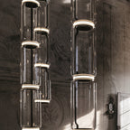Several cylinder clusters from this Clérachic pendant hang at staggered heights against a weathered fresco wall.