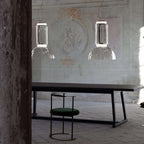 Two small square-edged Clérachic pendants hang above a stone bench and green stool in a weathered courtyard.