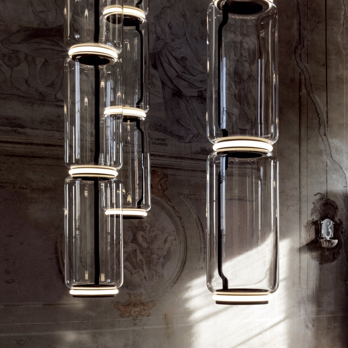 Multiple cylinder stacks of varying height from this Clérachic pendant cluster against a fresco wall.