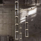Two cylinder stacks from this Clérachic pendant catch streaks of sunlight against a fresco wall.