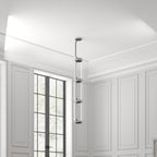 A stack of glowing cylinders from this Clérachic pendant hangs in a white-panelled room corner near a window.