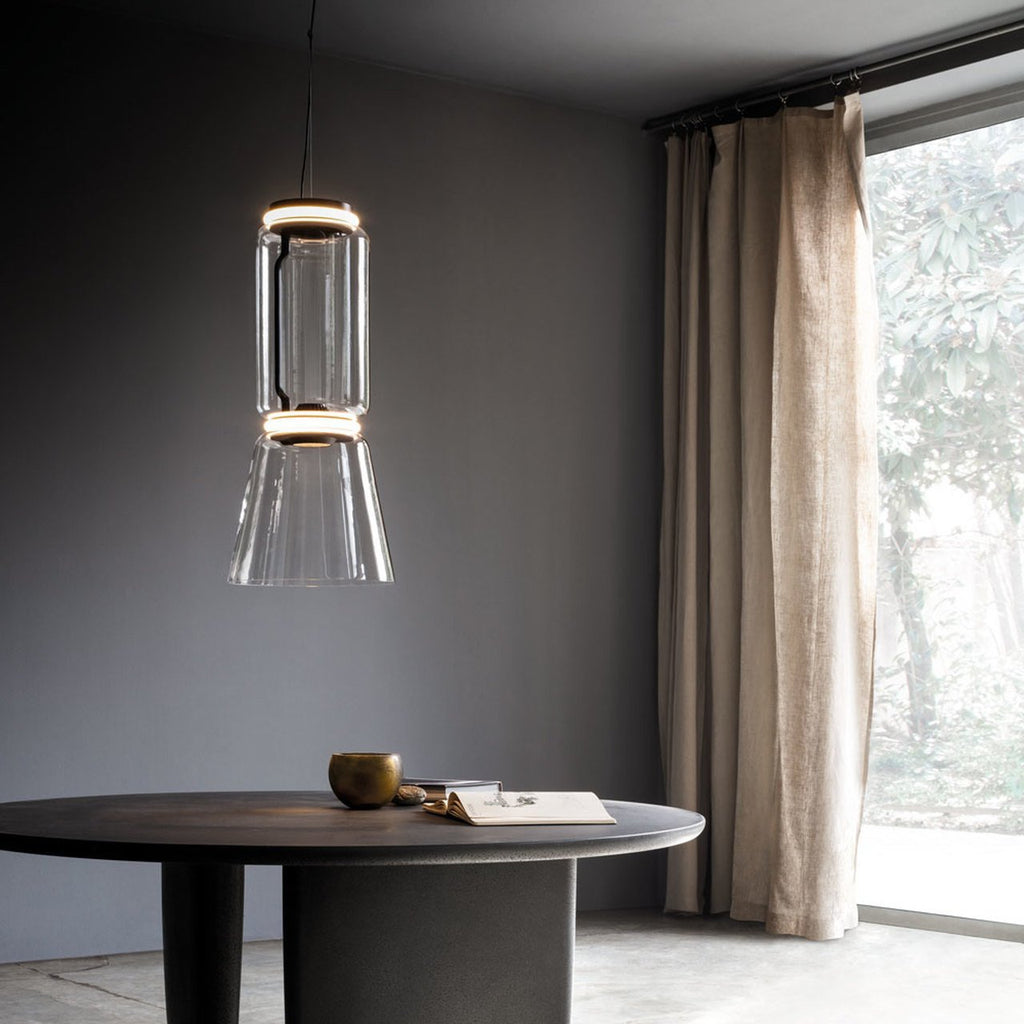 This Clérachic pendant's tapered clear-glass shade glows warm against a dark wall beside a floor-length curtain.