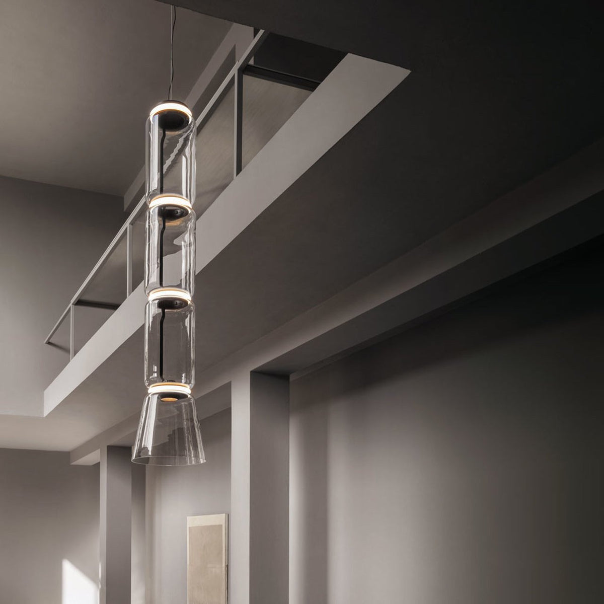 A stack of glass cylinders above a flared cone base on this Clérachic pendant glows warm over a glass stair rail.