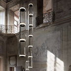 A row of glowing cylinder stacks from this Clérachic pendant hangs between wrought-iron balconies in a frescoed hall.