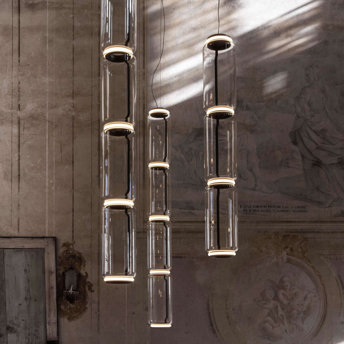 Close view of three staggered cylinder stacks from this Clérachic pendant against a frescoed wall.