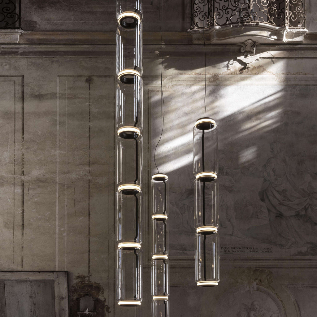 Two tall stacks of glowing glass cylinders from this Clérachic pendant hang in a frescoed period hall.