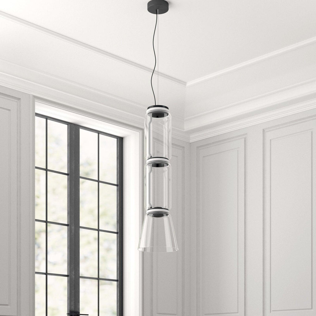 This Clérachic pendant's unlit cylinder-and-cone shade hangs in a white-panelled room beside a tall window.