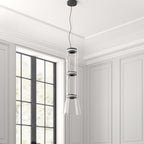This Clérachic pendant's unlit cylinder-and-cone shade hangs in a white-panelled room beside a tall window.