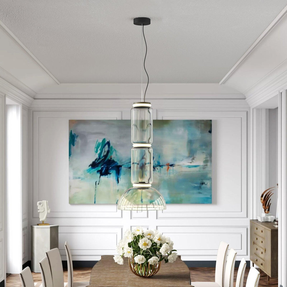 This Clérachic pendant hangs in stacked clear-glass cylinders above a dining table, beside an abstract canvas.