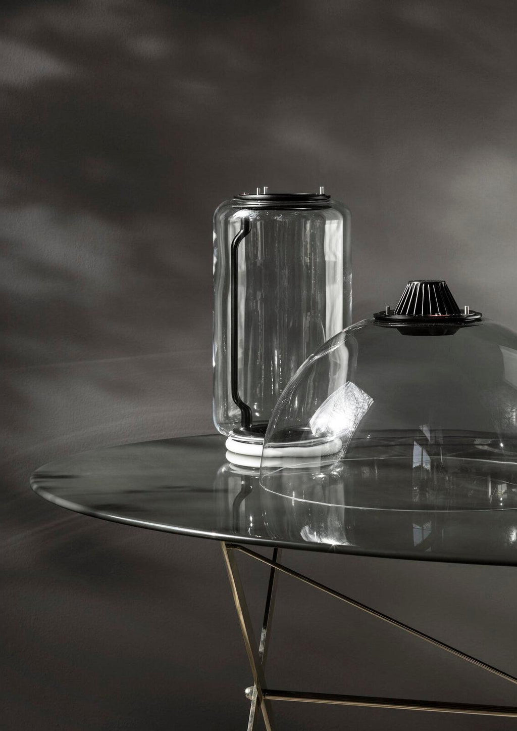 Close view of one glass cylinder from this Clérachic pendant resting on a glass table, fitted with its black LED cap.