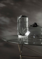 Close view of one glass cylinder from this Clérachic pendant resting on a glass table, fitted with its black LED cap.