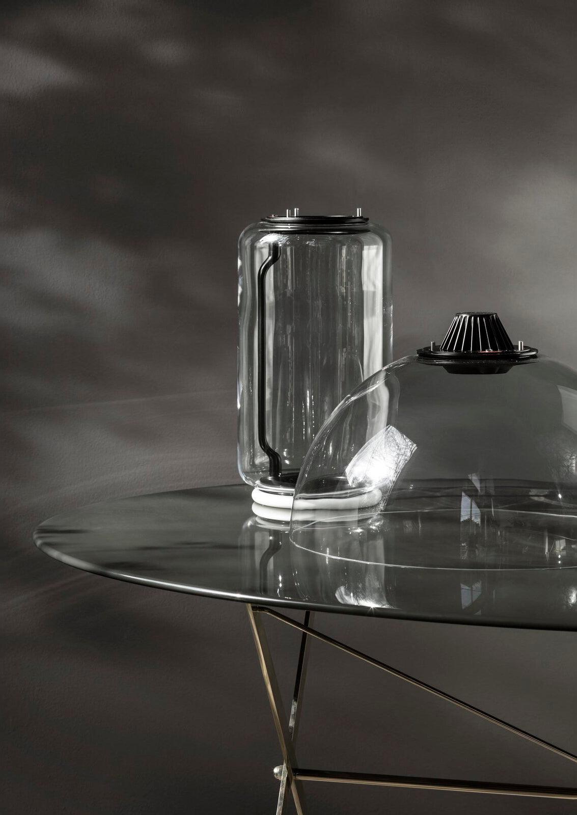 Close view of one glass cylinder from this Clérachic pendant resting on a glass table, fitted with its black LED cap.