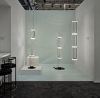 In a pale blue showroom, this Clérachic pendant's cylinder stack hangs beside freestanding glass fixtures.