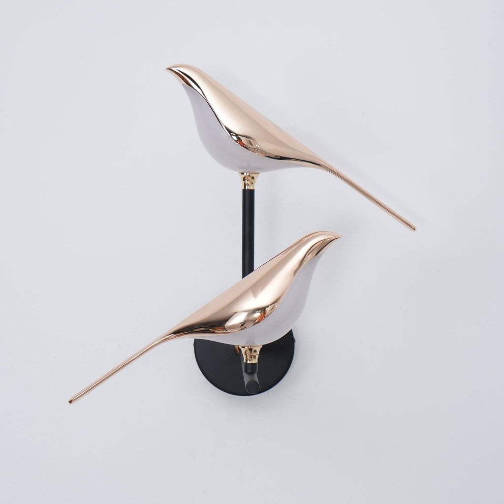 Black and rose gold Nomi bird wall lamp on a pale interior wall