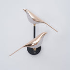 Black and rose gold Nomi bird wall lamp on a pale interior wall