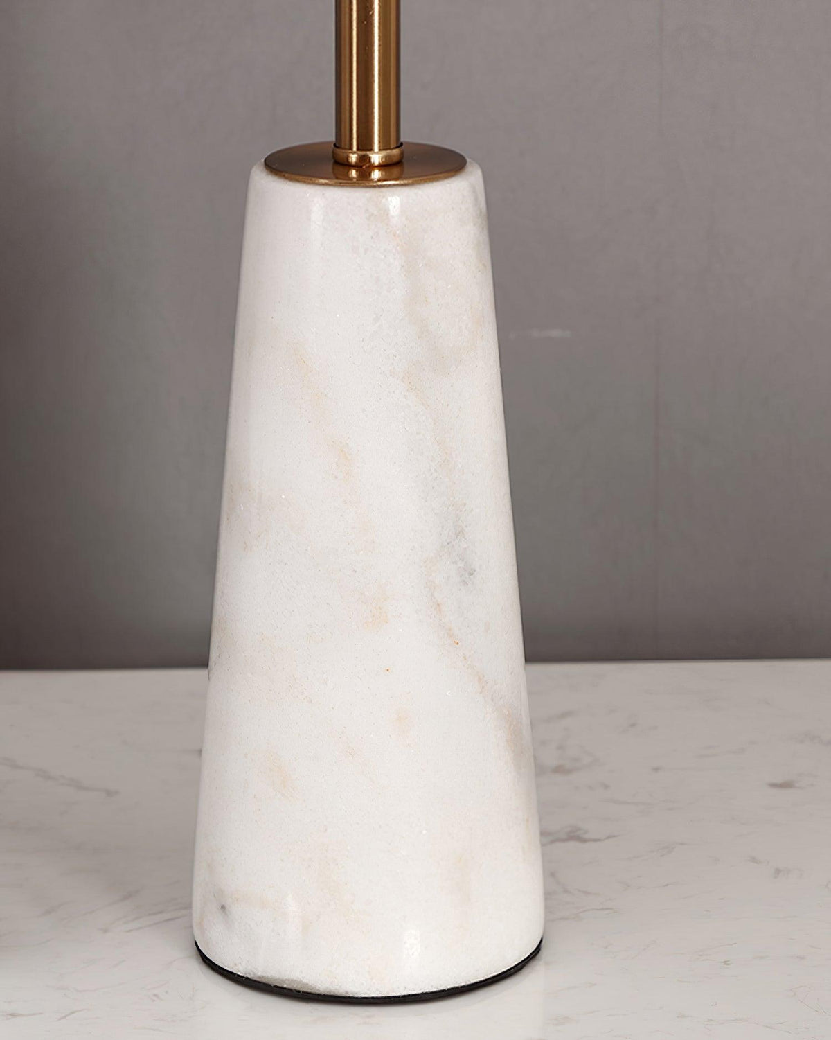 Close-up of the full faceted marble base of the Clérachic table lamp, veining visible against a plain wall.