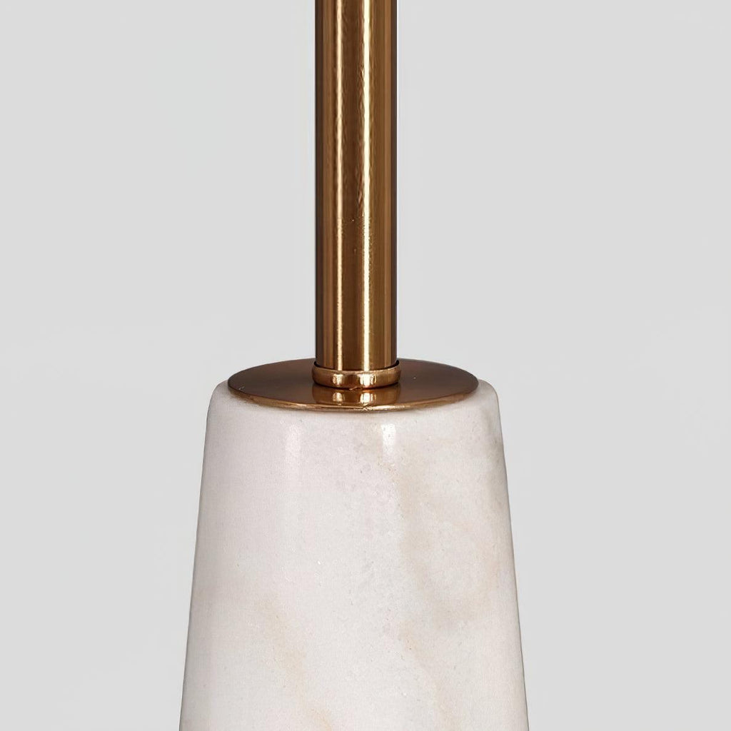 Close-up of the Clérachic table lamp's polished gold stem meeting its faceted marble base.