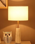 Clérachic lamp glowing warm at night beside the owl figurine, its drum shade lit against an amber-toned wall.