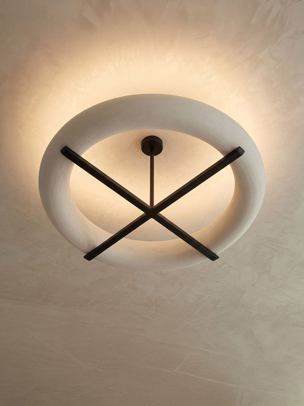 A tight view of this Clérachic ceiling light's oval shade and crossed stem, glowing warm against the ceiling.