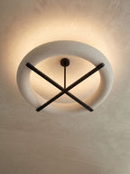 A tight view of this Clérachic ceiling light's oval shade and crossed stem, glowing warm against the ceiling.