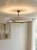 Near a curtained window, this Clérachic ceiling light in black casts its warm glow across a plaster-textured ceiling.