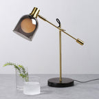Clérachic brass table lamp beside a glass vase of foliage and a frosted glass votive, styled on a pale grey stone surface.