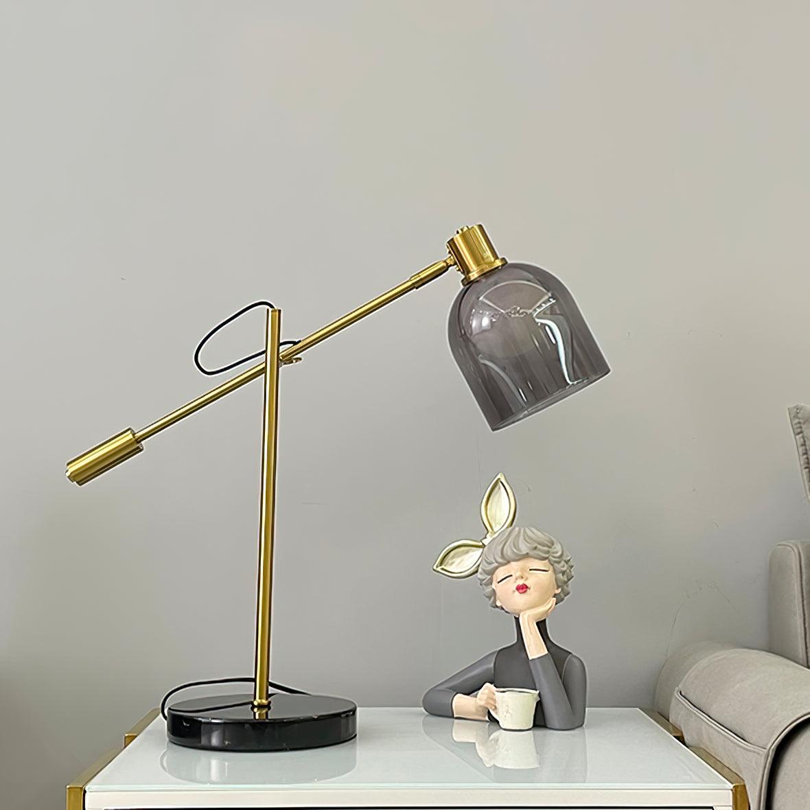 A seated figurine holding a teacup shares a glossy white table with the Clérachic brass table lamp, its cord looped at the base.