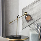 An angled grey and white wall panel backs the round gold-trimmed side table holding the Clérachic brass table lamp.