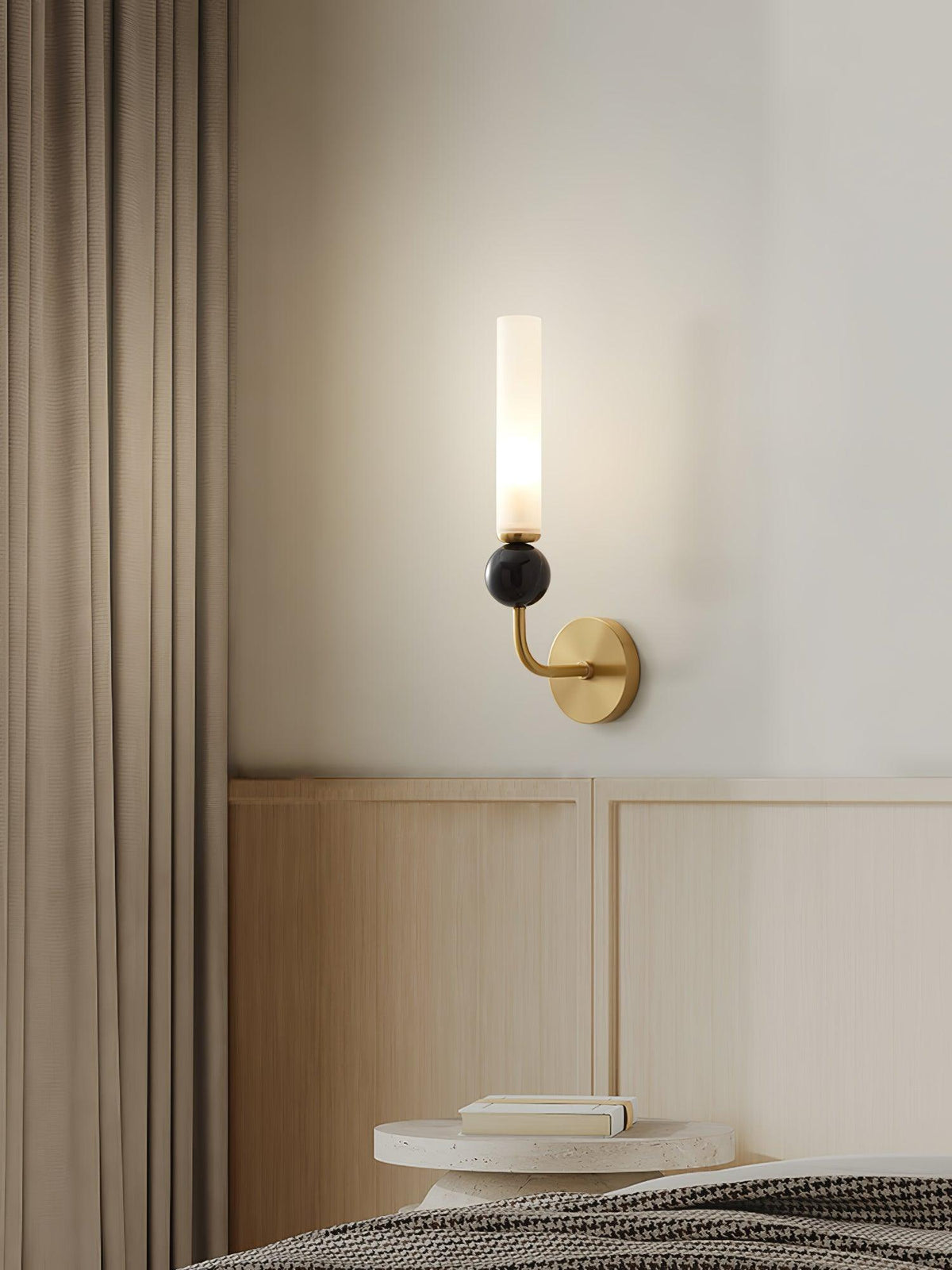 A Clérachic black wall sconce lights a bedside table stacked with books, set against a dark curtain beside the headboard.