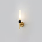 A Clérachic brass-arm wall sconce with a black marble orb, lit and shown front-on against a plain grey studio background.