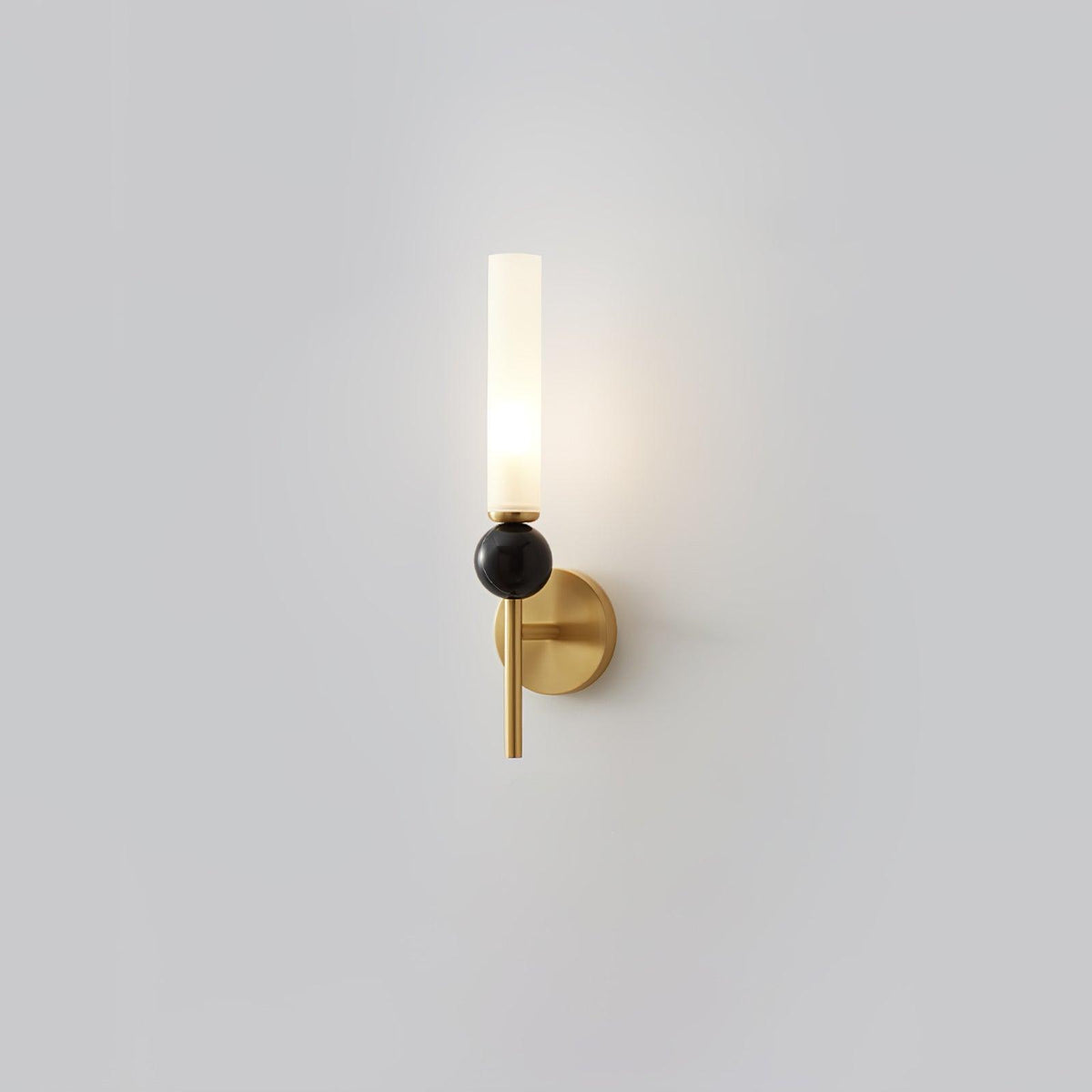 A Clérachic brass-arm wall sconce with a black marble orb, lit and shown front-on against a plain grey studio background.